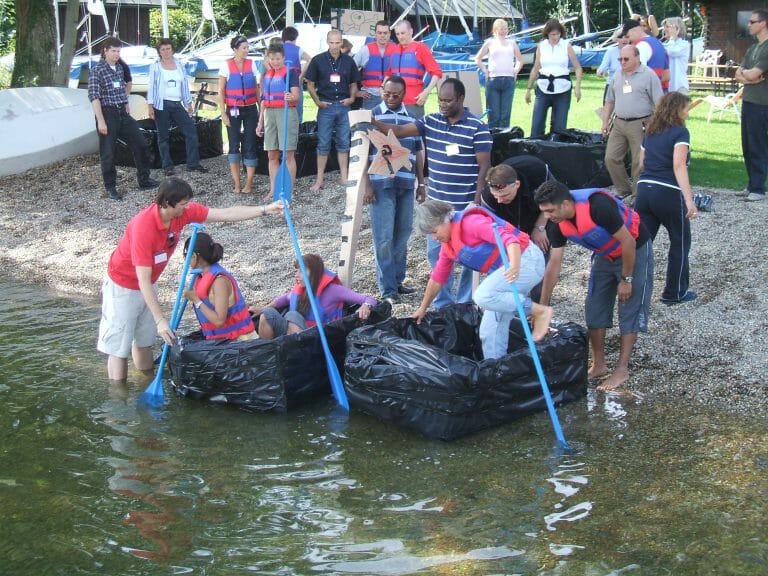 Delegates getting into & standing beside a cardboard boat they built during their team-building activity with Orangeworks.