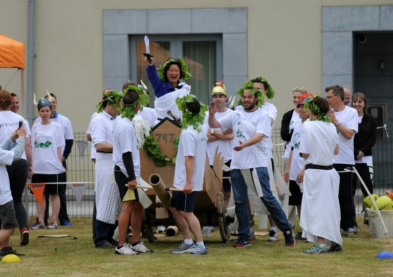 Happy team smiling and laughing, wearing roman clothing, after winning their chariot race during their team building event.