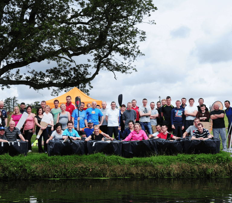 Delegates standing beside the cardboard boats they built and designed during Flat Out Afloat, a corporate team-building game.