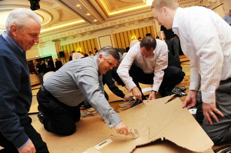 Delegates working together cutting cardboard for the pyramid they are building for their Orangeworks team building activity.