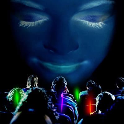 Delegates sitting in a cinema-style room holding glowsticks with an image of a women's face on the screen in front of them.