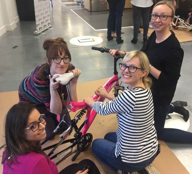 Team smiling with their newly built bike for charity during Orangeworks team building activity Charity Bike Build.