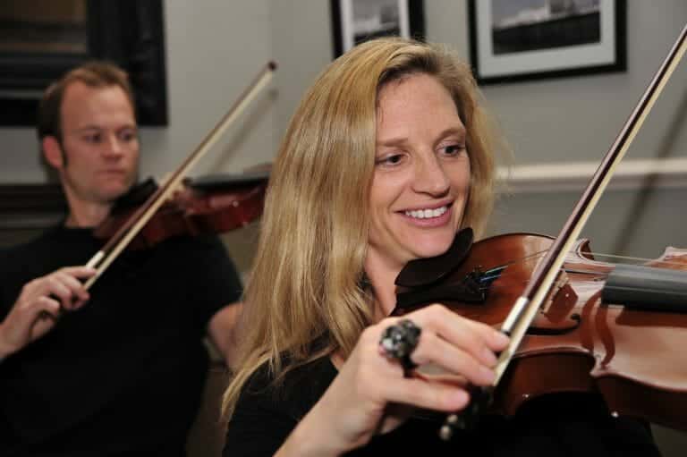 A woman holding her violin practising the cords for the final performance of Orchestrate. A man behind her doing the same.