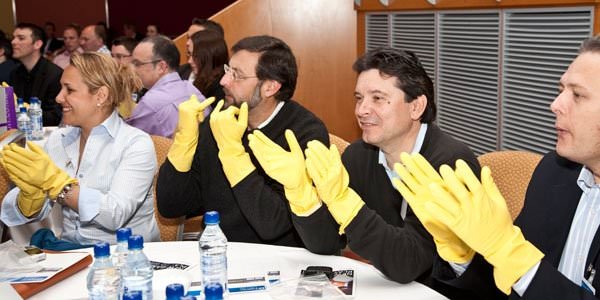 Delegates sitting at a table wearing yellow gloves while making music with gloves during an Orangeworks corporate energiser.