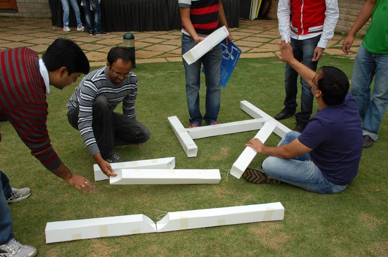 Colleagues working together putting pieces of cardboard together to make a giant puppet during their team bonding activity.