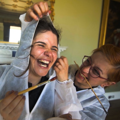 Delegates wearing white overalls holding paintbrushes while laughing as they prepare for a creative team building activity