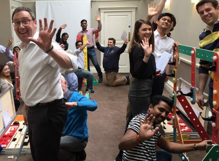 Delegates smiling with hands in the air while building their mechanical contraption, as part of their team-building workshop with Orangeworks