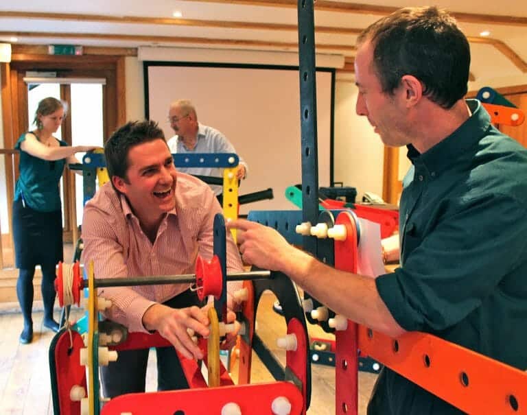 Delegates laughing and chatting together while they build their contraption as part of Orangeworks experiential activity called Plan of Acrion.