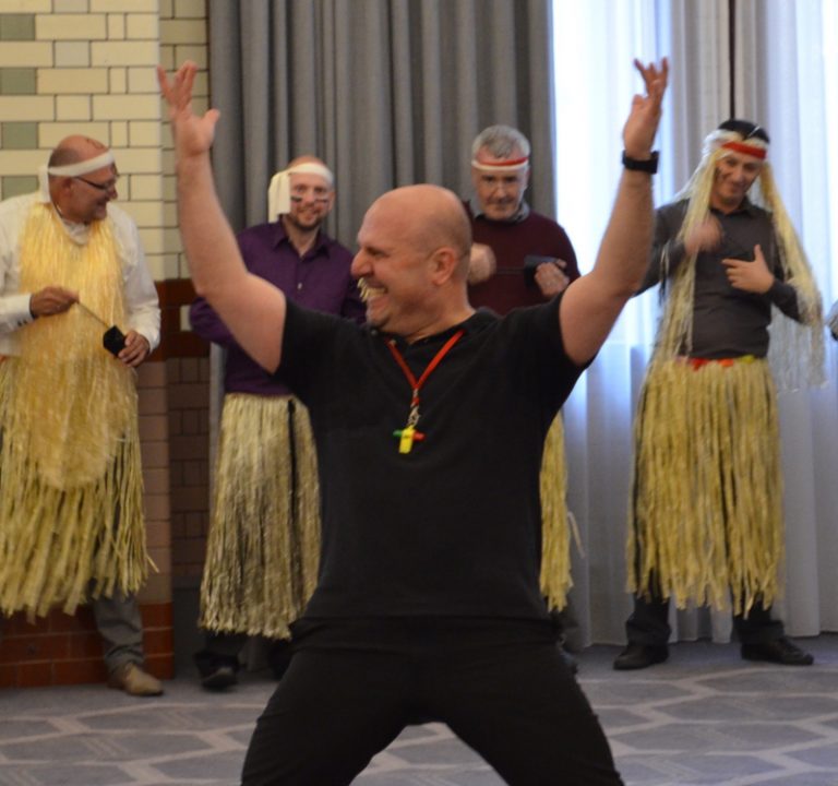 Ed Freitas, Orangeworks haka instructor, with his hands in the air, with delegates behind him wearing hula skirts.