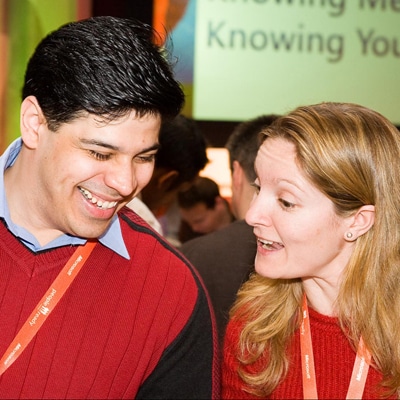 Two people smiling wearing red jumpers chatting to each other during an icebreaker conference by Orangeworks called Knowing Me Knowing You.