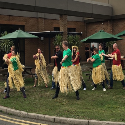 Team wearing straw hula skirts while learn to do the haka with Orangeworks