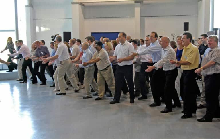 Male participants of One Voice, the team conference ice-breaker, standing in a line all doing dance move with their hands.