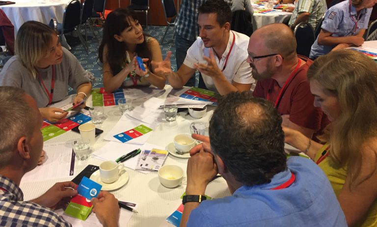 Delegates sitting around a table discussing their product idea for Global Innovation Game, a fun team building challenge.