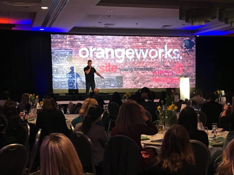 Dean the Beatboxer standing on stage at an AIPCO corporate team-building event, teaching a group of delegates how to beatbox.