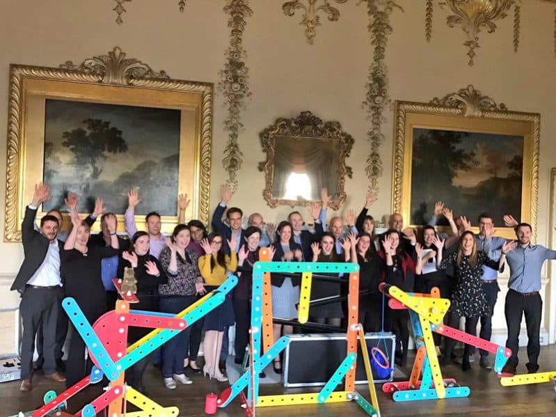 Delegates smiling with their hands in the air with their Plan of Action contraption they created during their company away day.