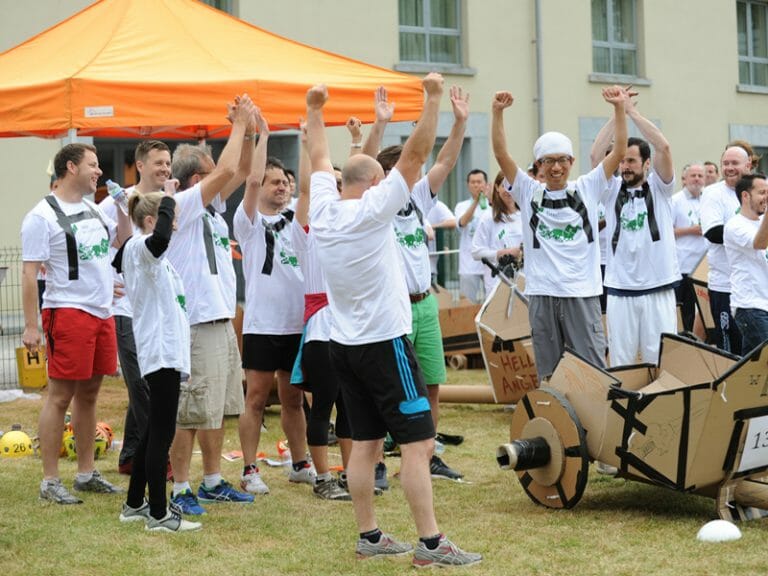 A team cheering with their hands in the air after winning Flat Out Chariot Racing, a creative team building activity.