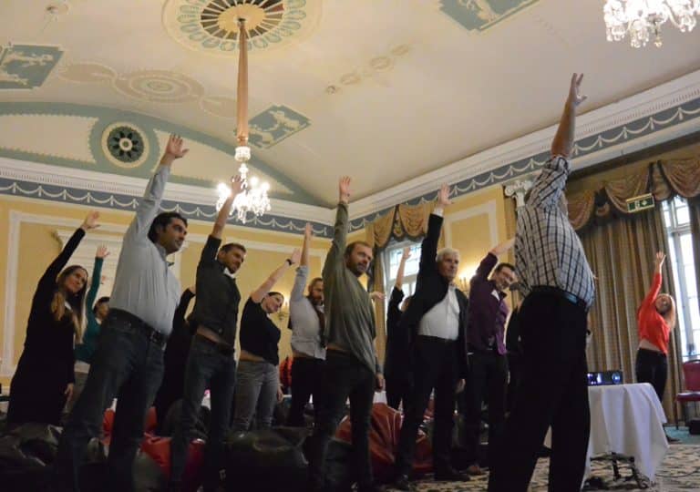 A team standing with their hand in the arm as they re-energise during Meditainment, a corporate wellness team building event.