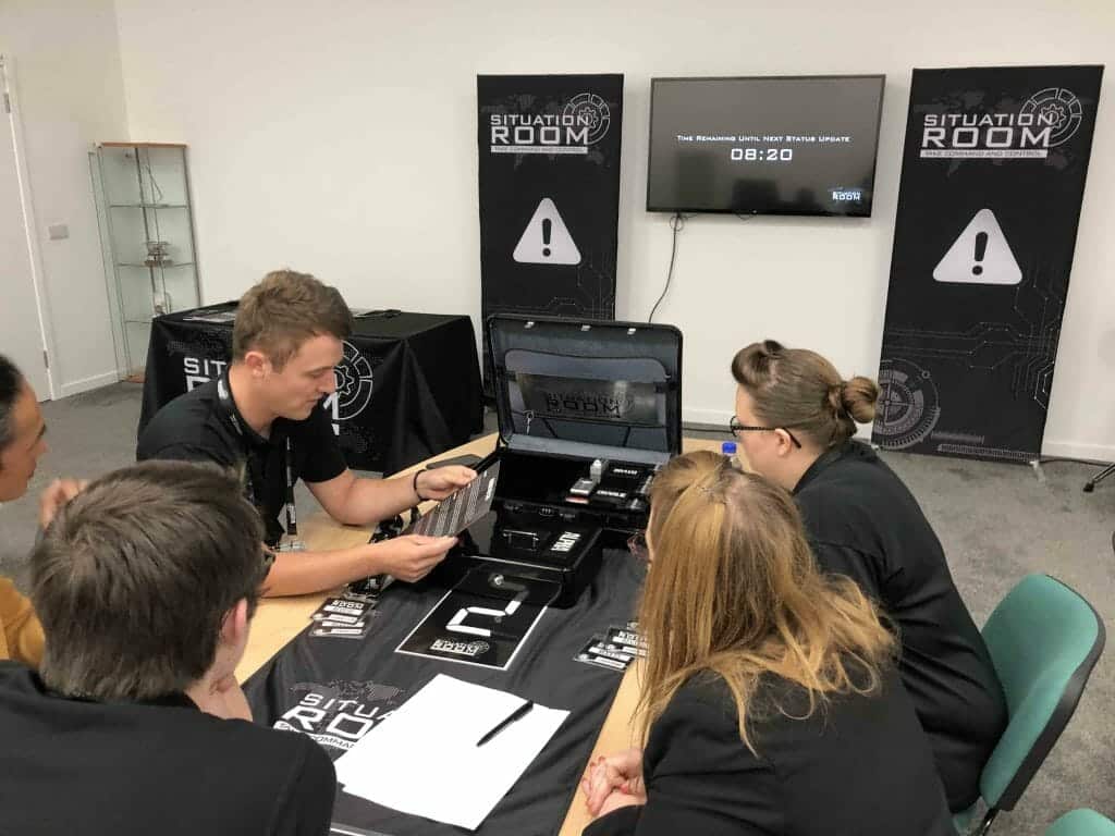 a team of delegates in the situation room sitting around a table examining the equipment. with an open brief case.