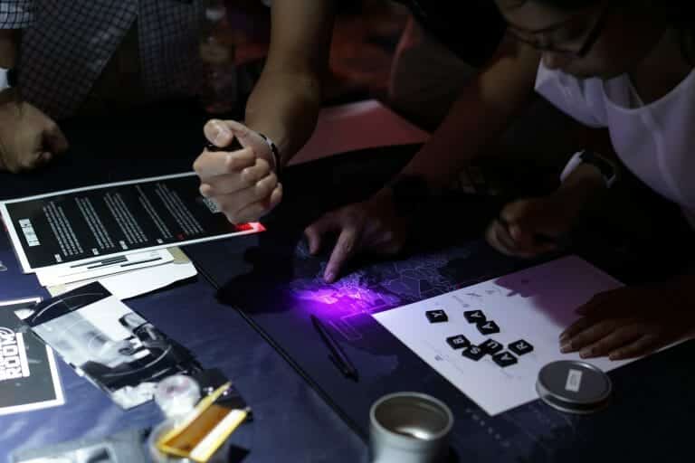 delegates in the situation room looking over a table with a map, a torch, jars, a pen, documents and photos on it.