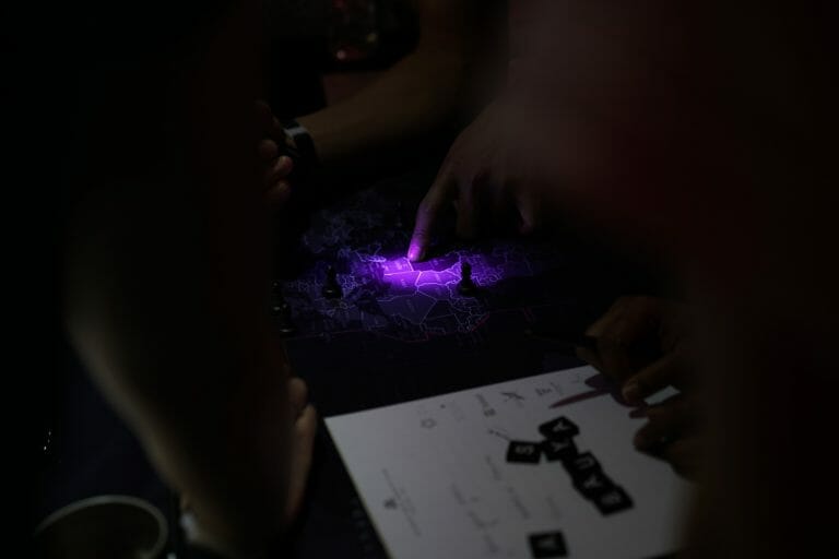 A team of people working on a map in the situation room. paper, counters and a pencil to the side of the map.