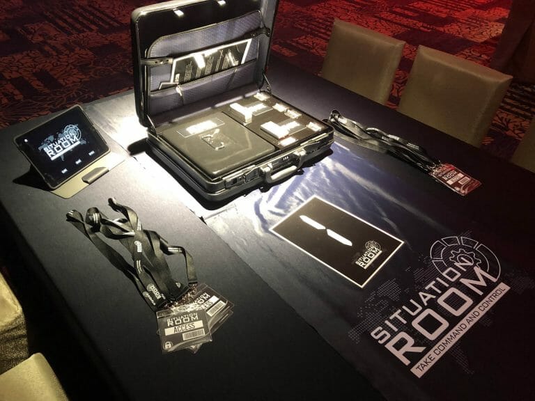 team building situation room with equipment played out on the table, including an open brief case, an iPad and lanyards.