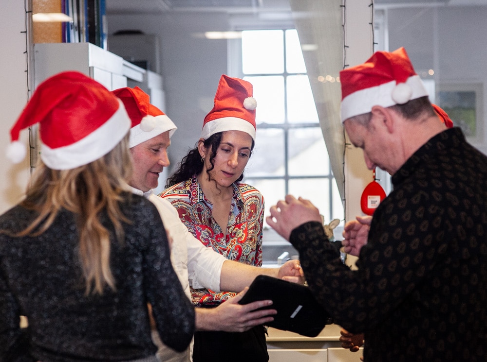 Four delegates wearing Santa hats looking at an ipad. They are working together on a team building challenge called Quickfire Christmas by Orangeworks.