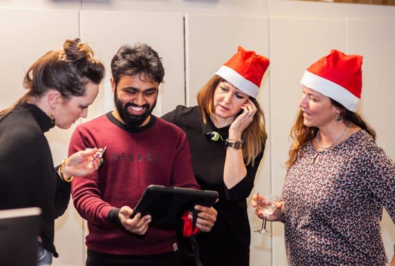 Four delegates standing together looking at an iPad. They are involved in a team building challenge called Quickfire Christmas by Orangeworks.