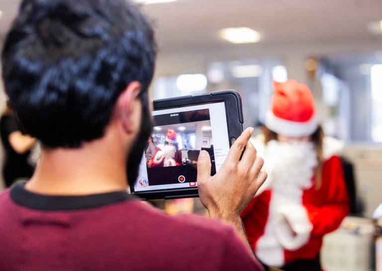 A man holding an ipad taking a photo of a woman in a Santa costume, as part of their Christmas themed team building activity with Orangeworks.