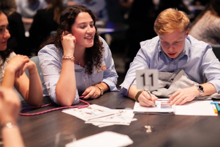 Delegates sitting at a table reading documents and instructions for Peak Performance, one of Orangeworks Team Development Activities.