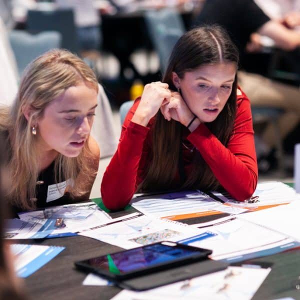 Two female delegates reading a number of documents that are the instructions for Peak Performance, one of Orangeworks Team Development Activities.
