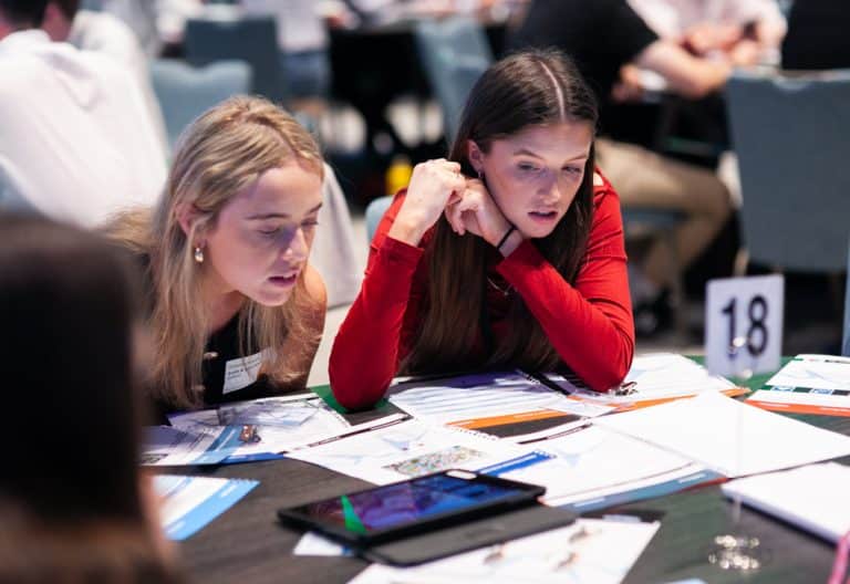 Two female delegates reading a number of documents that are the instructions for Peak Performance, one of Orangeworks Team Development Activities.