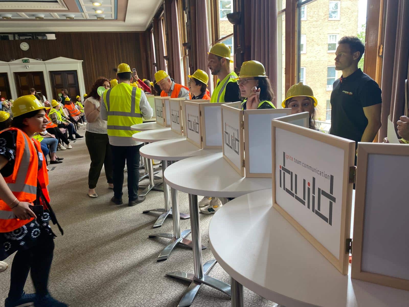 Delegates wearing builders hats and high vis jackets as they work together on Orangeworks innovative taem building activity, iBuild.
