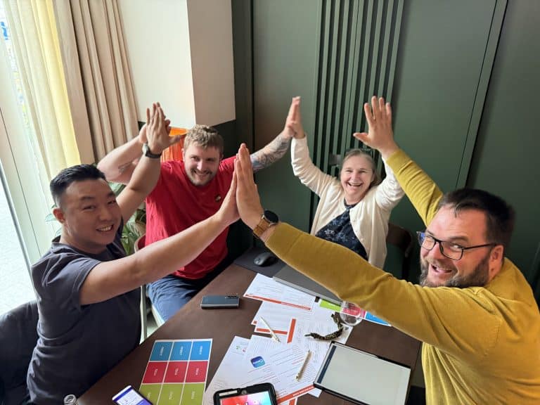 Delegates sitting in a circle at a table high fiving in unision during their Global Innovation Game AI Team Building Challenges with Orangeworks.