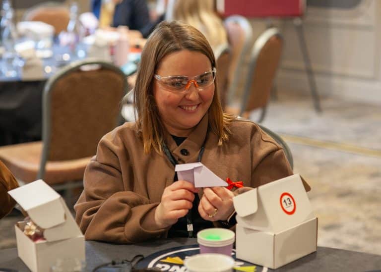 A delegate wearing safety goggles getting ready to fly her paper airplane that she made during Orangeworks Traitors inspired team building activity called Friend or Foe.