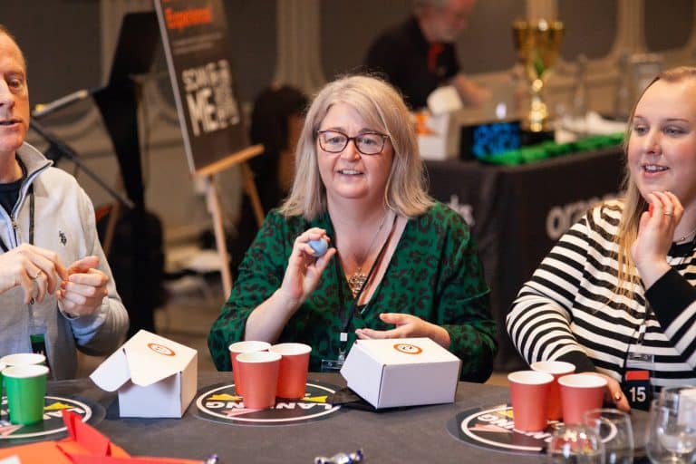 Delegates sitting down at a table playing a cups game as part of Orangeworks Traitors inpsired team challenge called Friend or Foe.